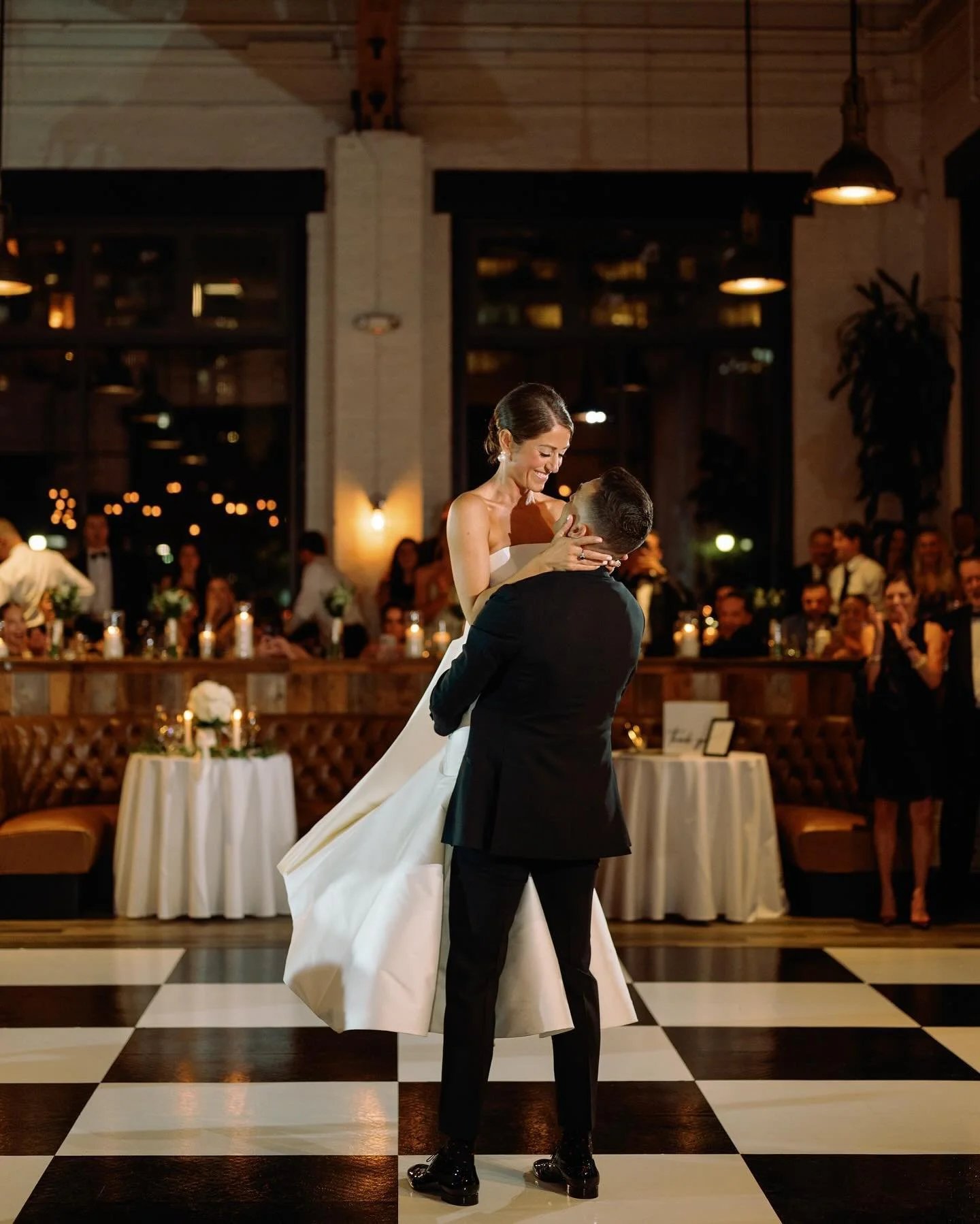 Groom lifting bride during their first dance on a checkered dance floor at an indoor Oklahoma City wedding venue