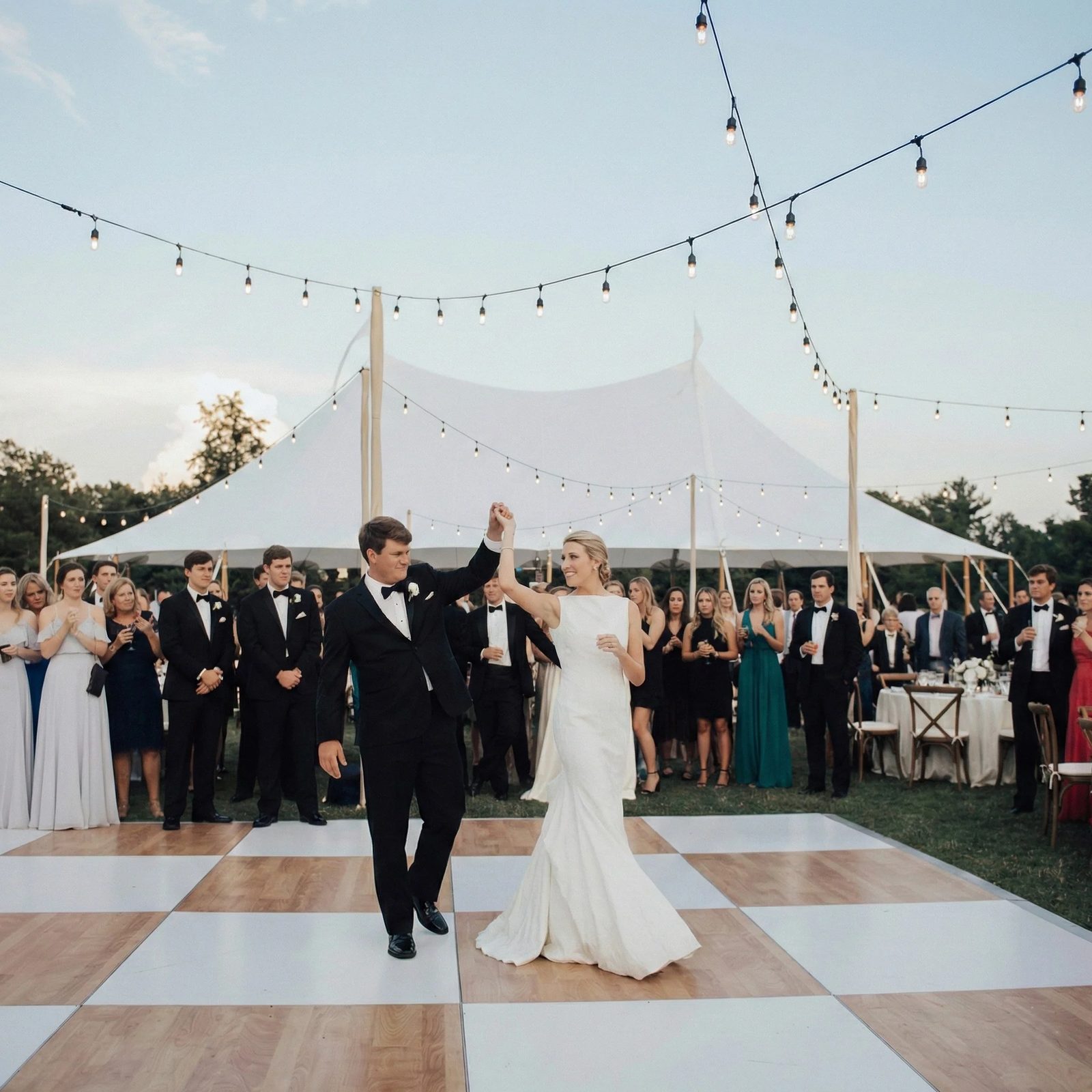 Couple dancing on a wood and white checkered dance floor under string lights at an outdoor tented Oklahoma City wedding reception